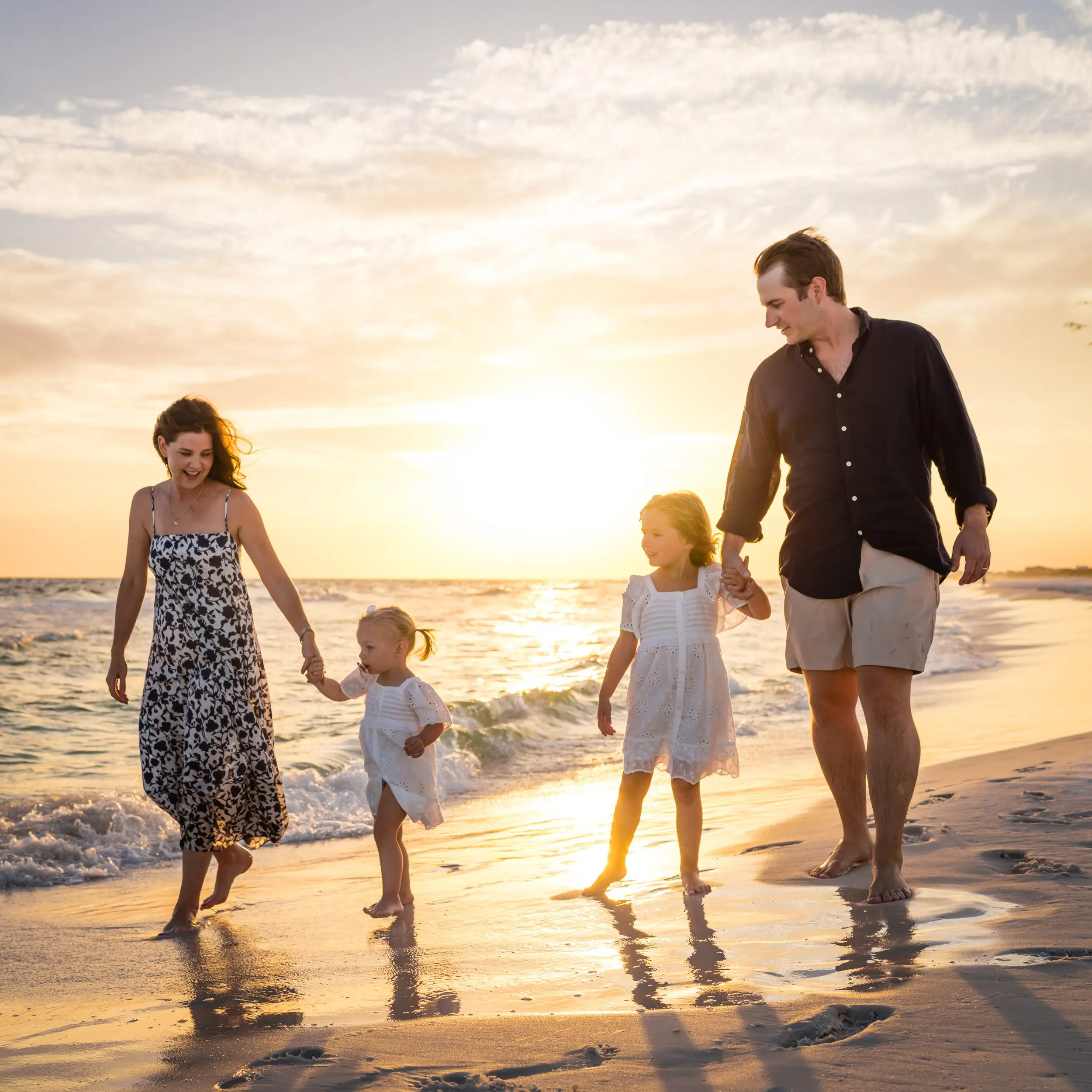 A family holding hands and walking along the shoreline at sunset.