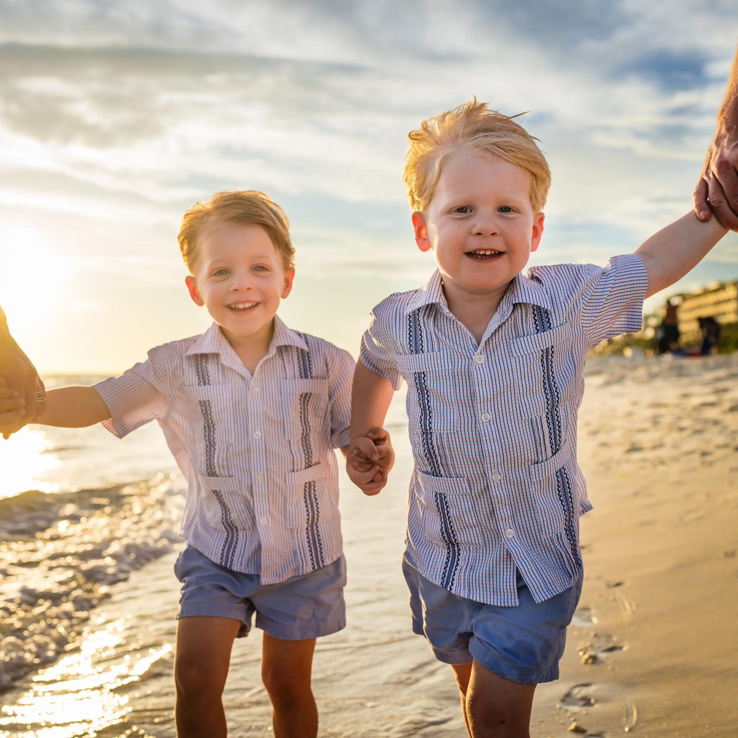 Two boys walking hand in hand with adults along the beach.