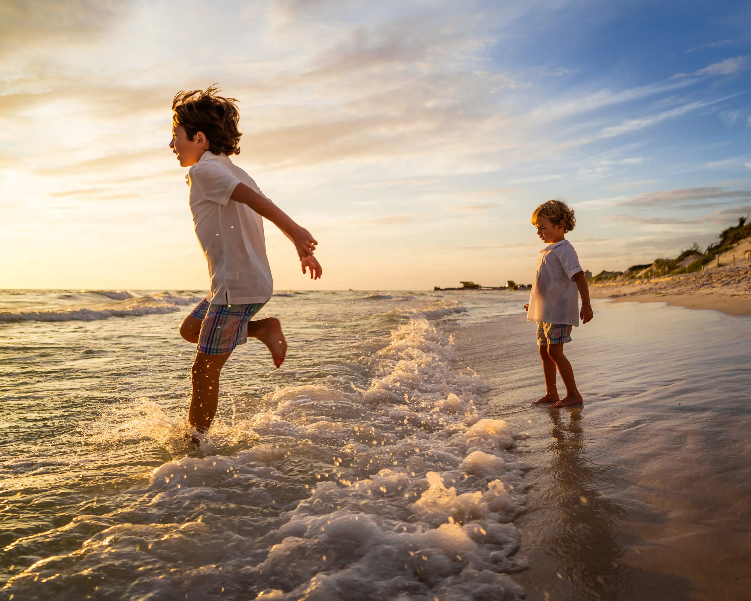 Two children jumping over the shallow surf at sunset.