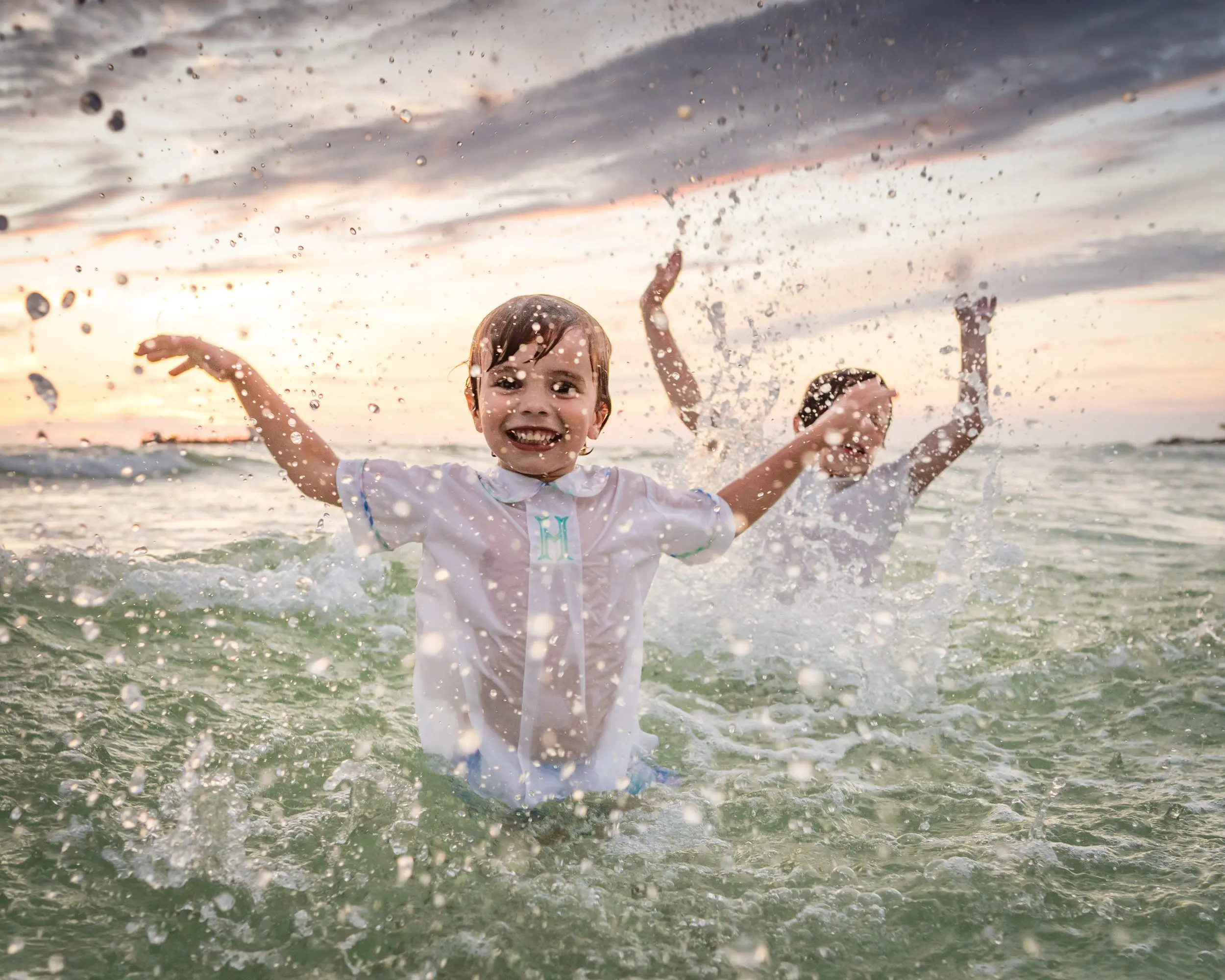 A child splashing water toward the camera at sunset.