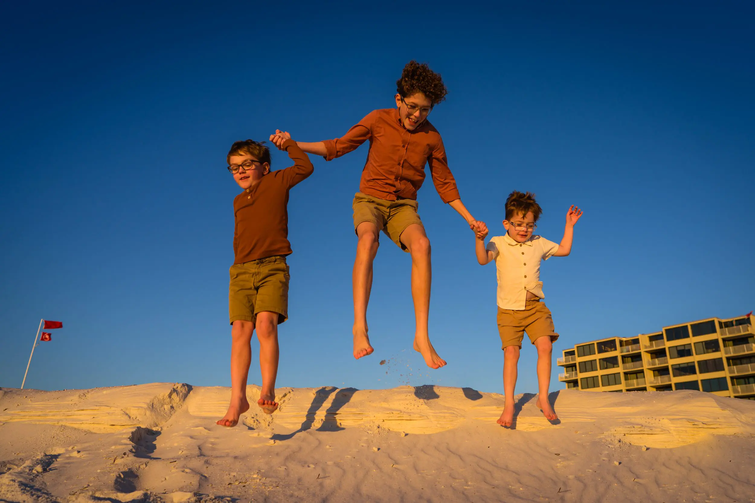 Three children jumping together on the beach in warm evening light.