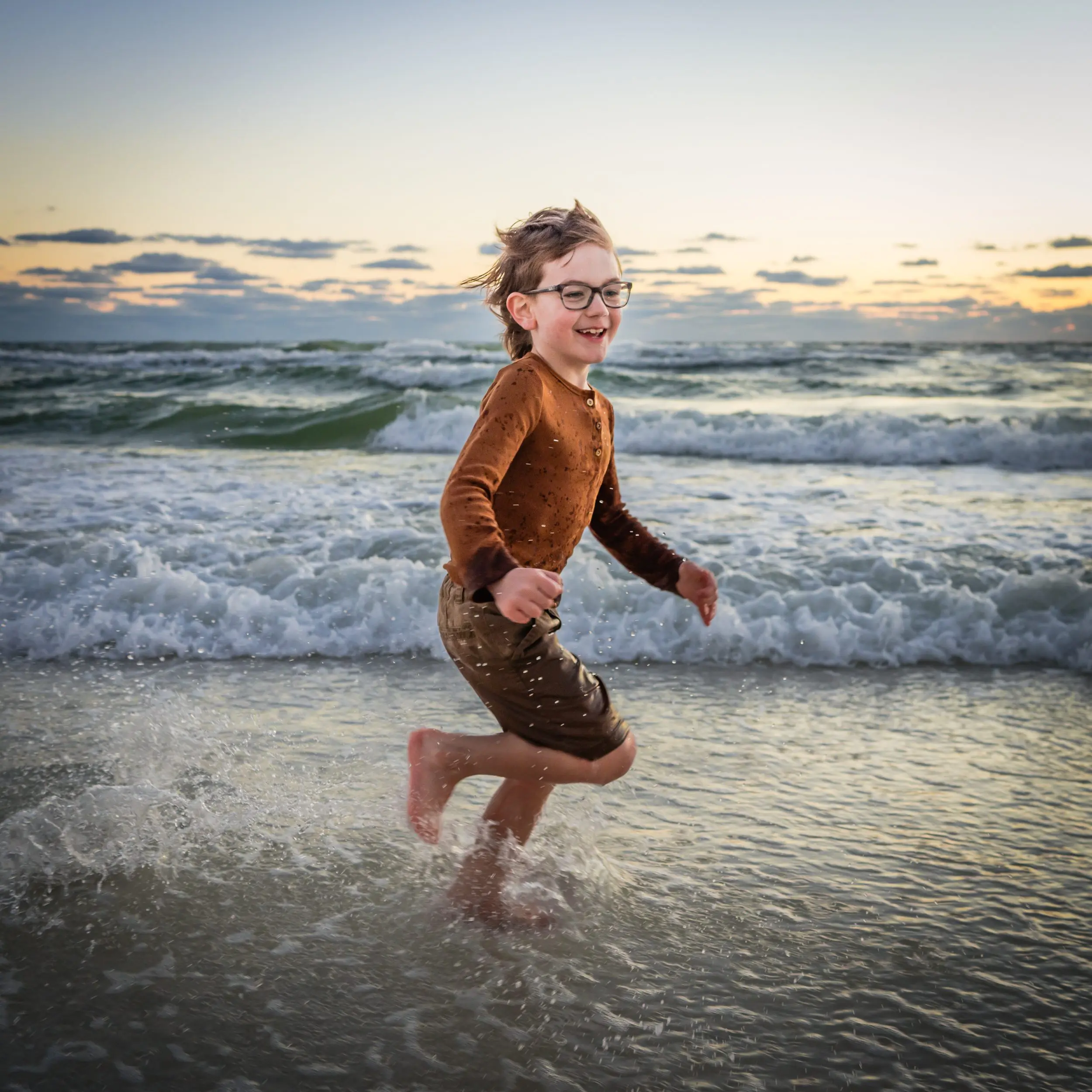 A child laughing while running through the surf.