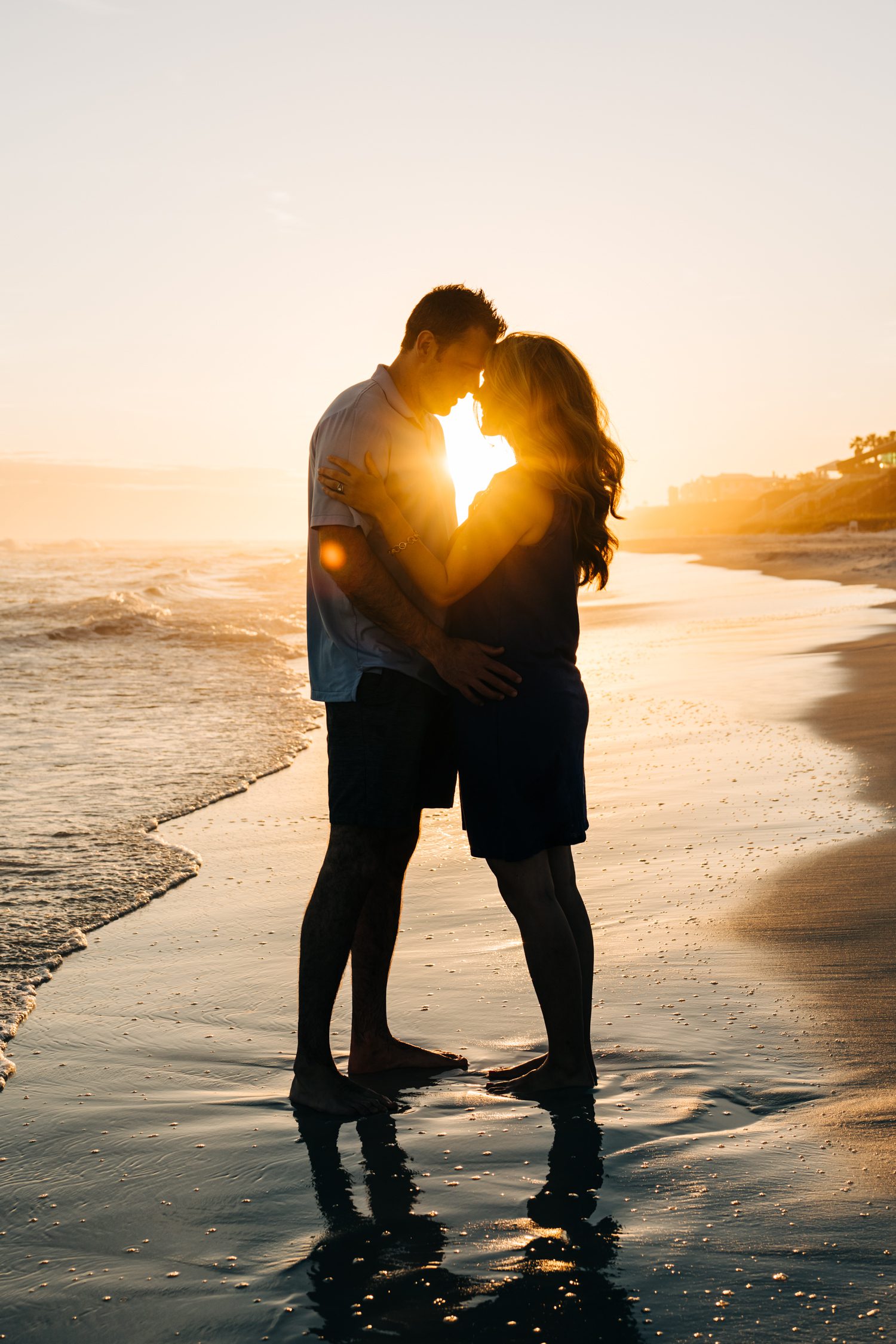 A couple embracing on the beach with sunlight between their faces.