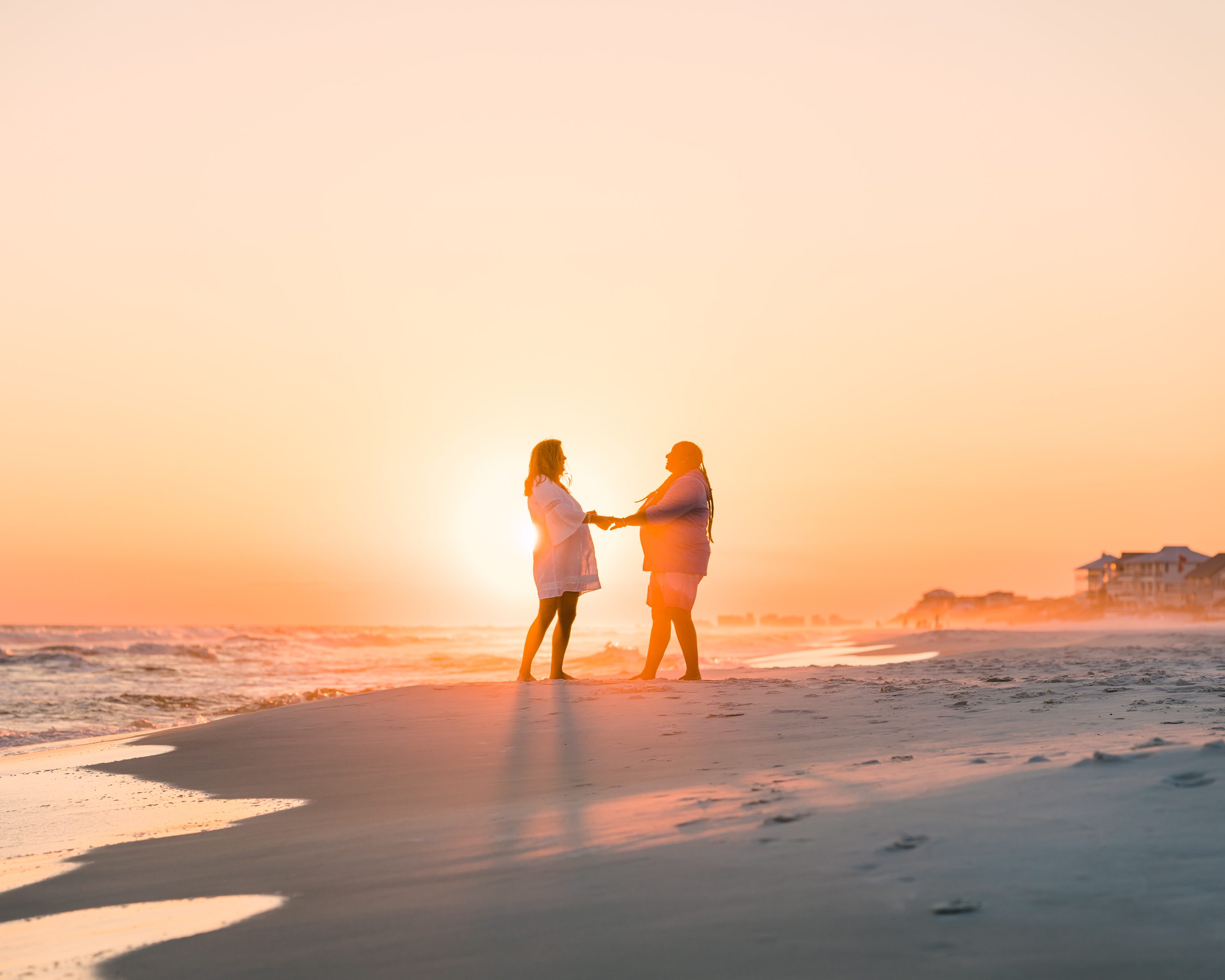 A couple holding hands on the beach in golden evening light.