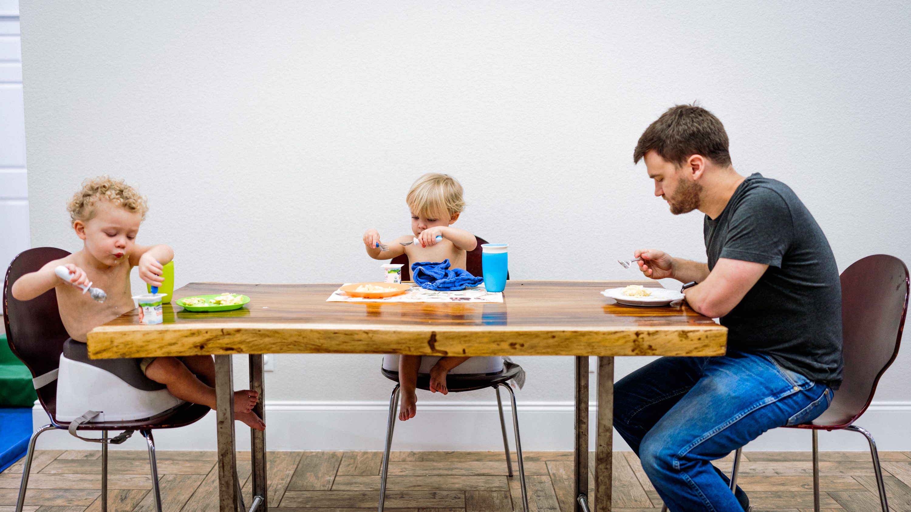 A parent and two young children sharing a meal around the kitchen table.