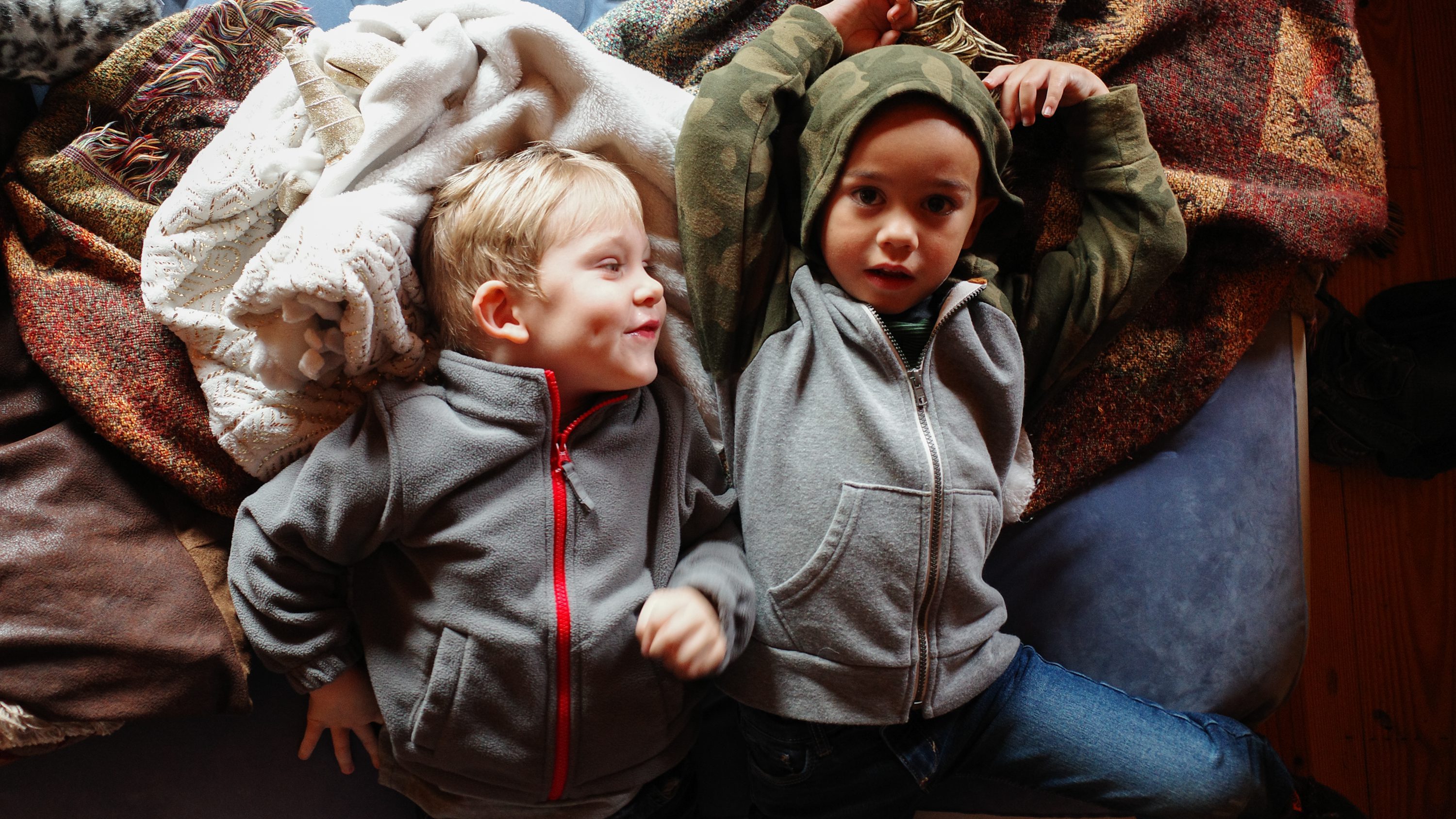 Two children lying together beside a pile of blankets.