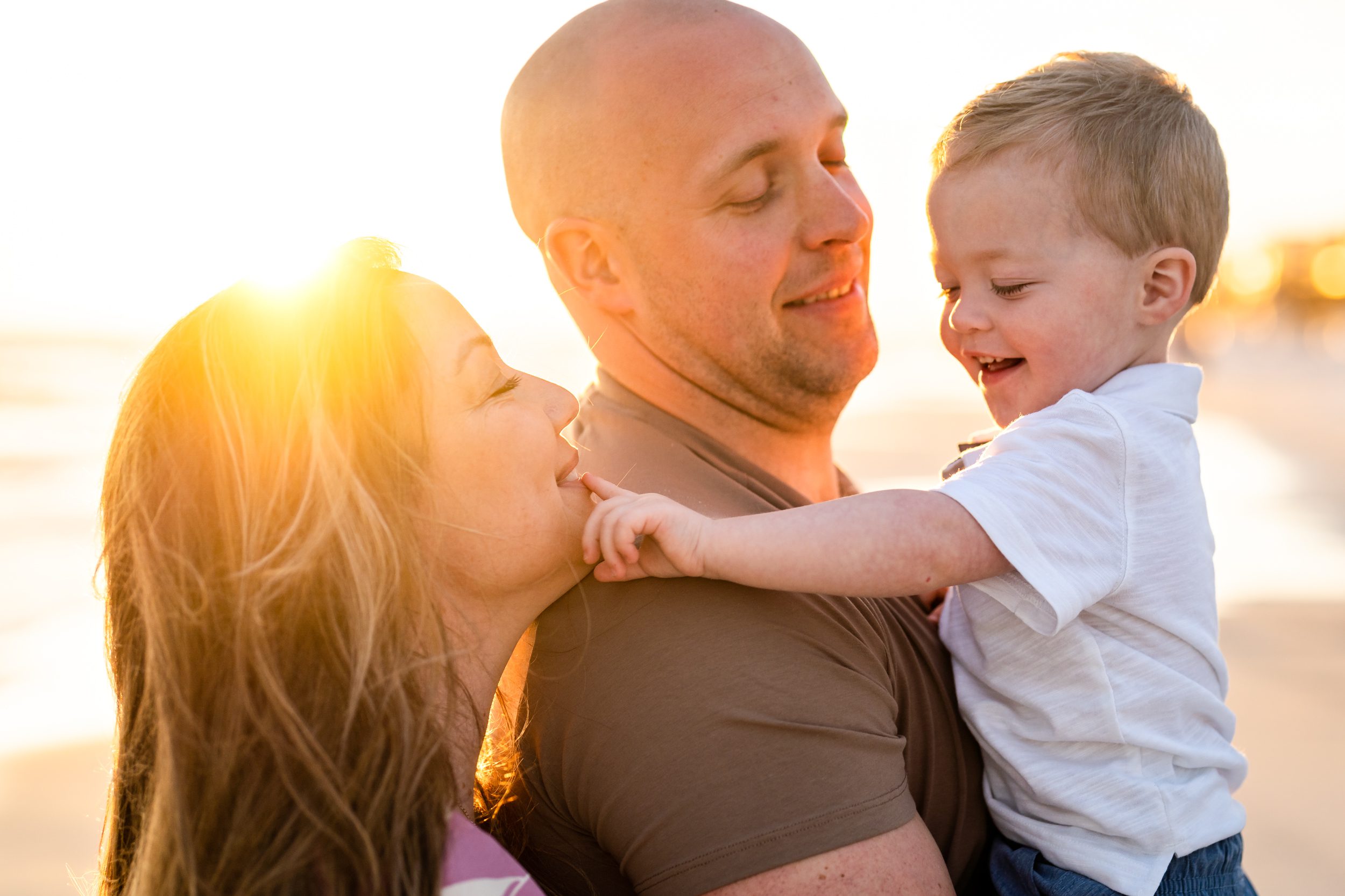 Two parents cuddling their young child in warm sunset light.
