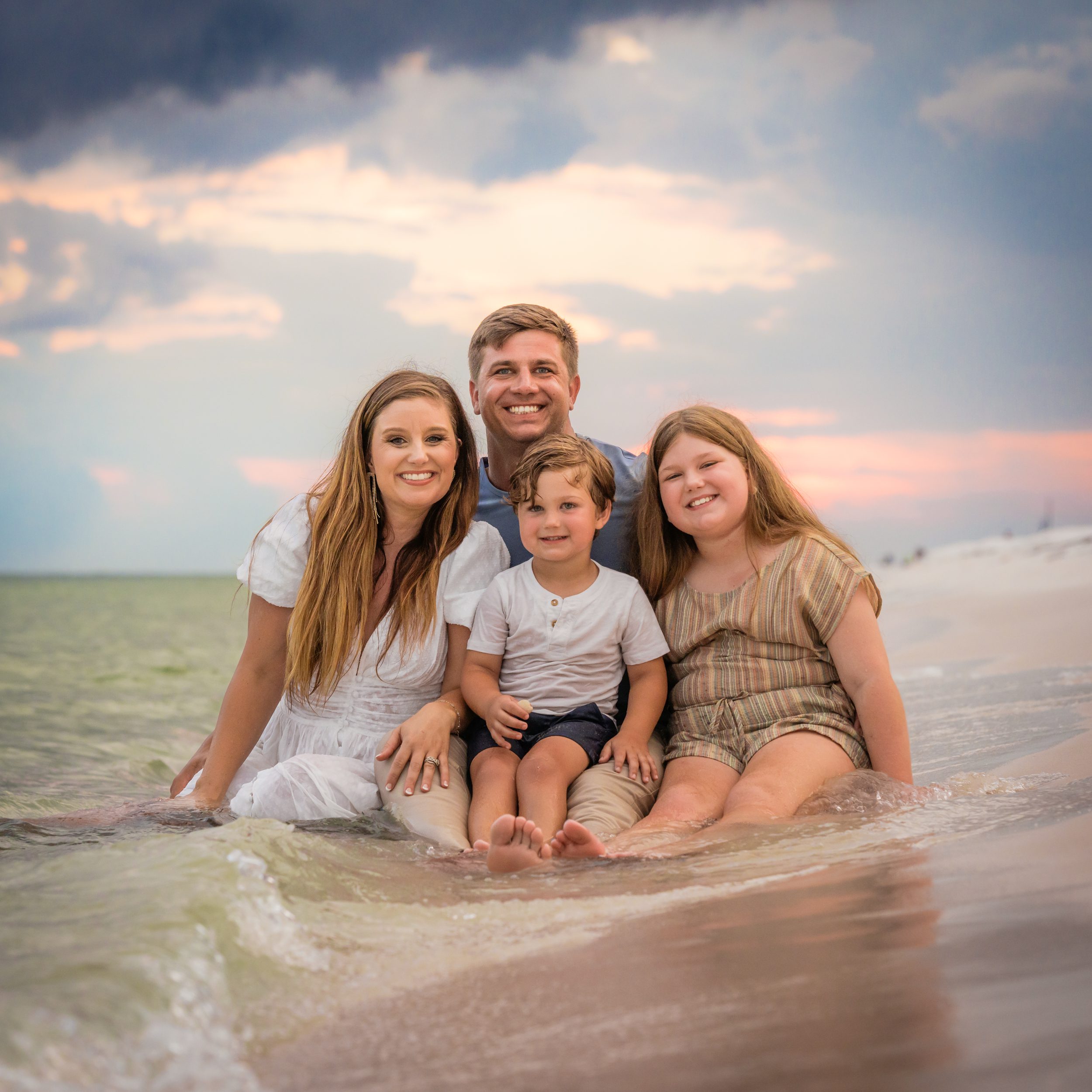 A family sitting together in the shallow surf.