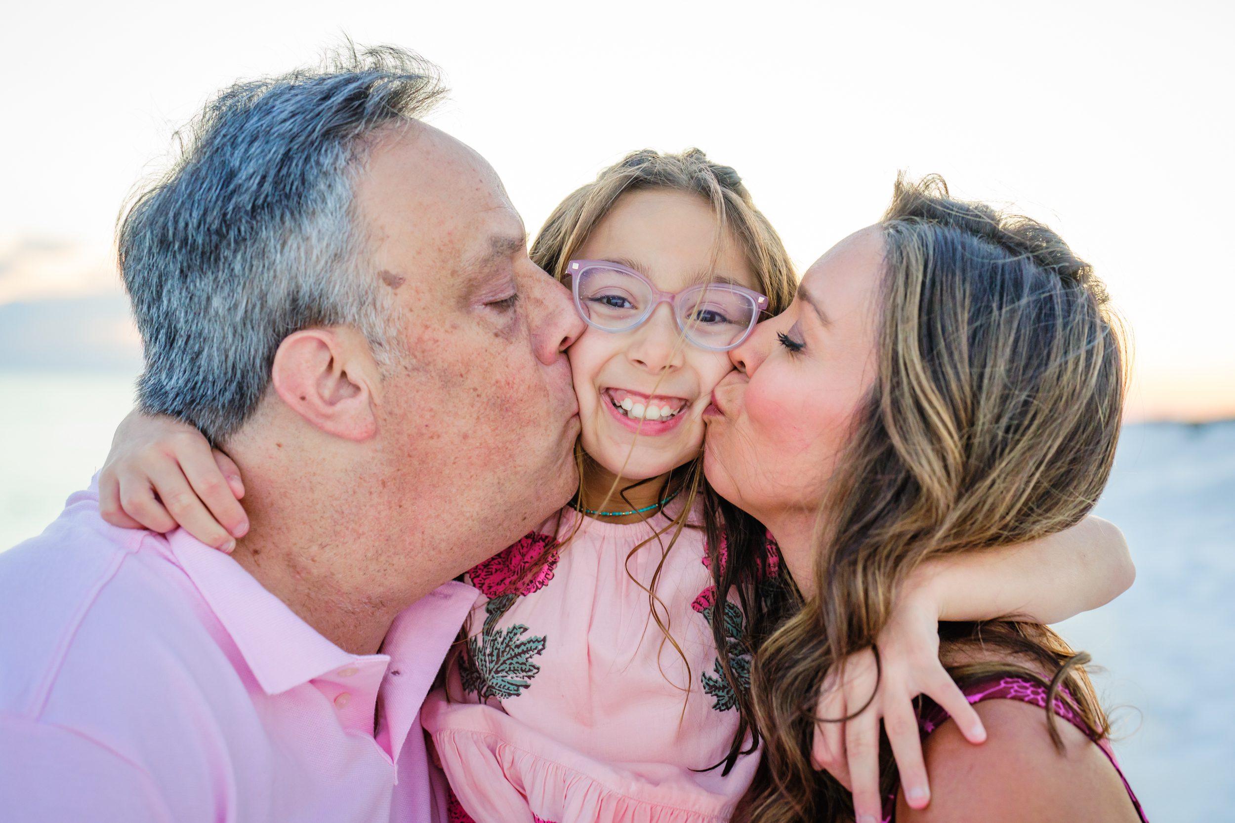 Two adults kissing a smiling child on the cheeks.