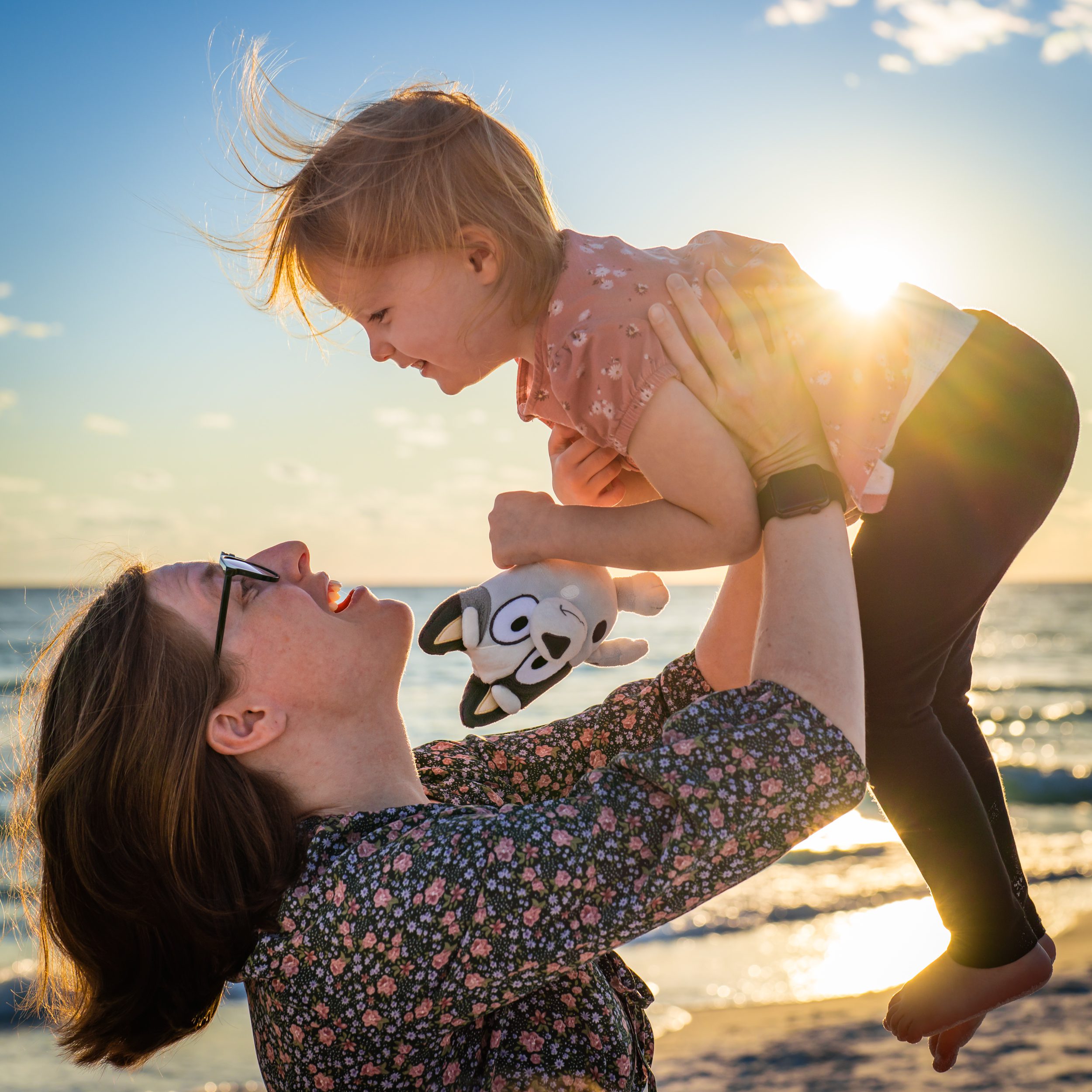 A parent lifting a laughing child into the sunset light.