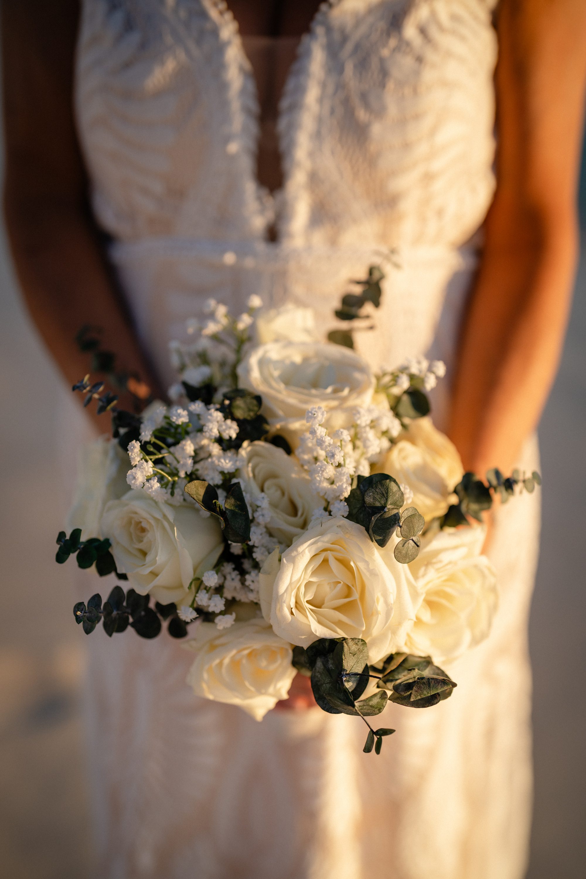 Close-up of a bride holding a bouquet of white roses and greenery.