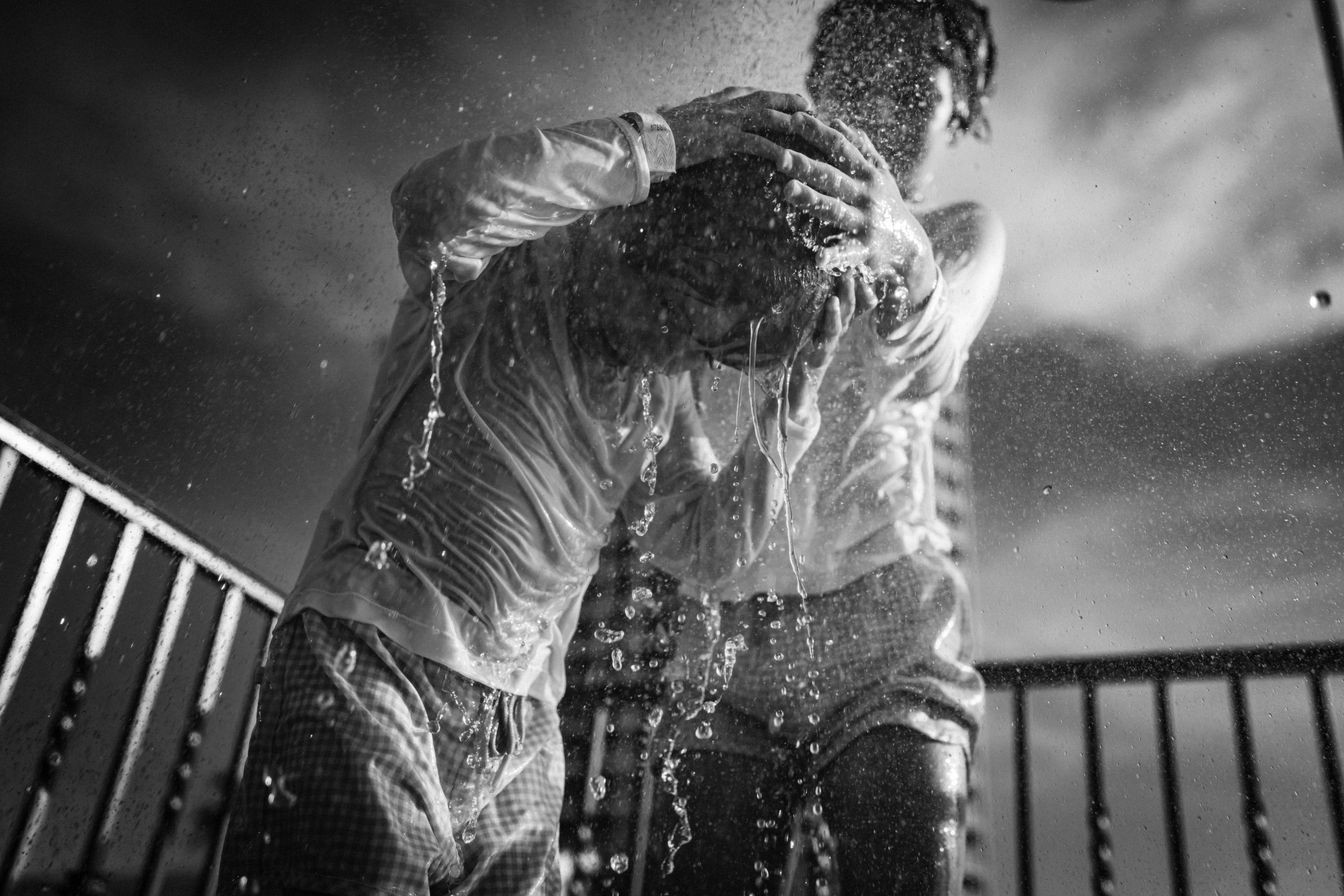 Black-and-white photograph of two people embracing beneath an outdoor shower.