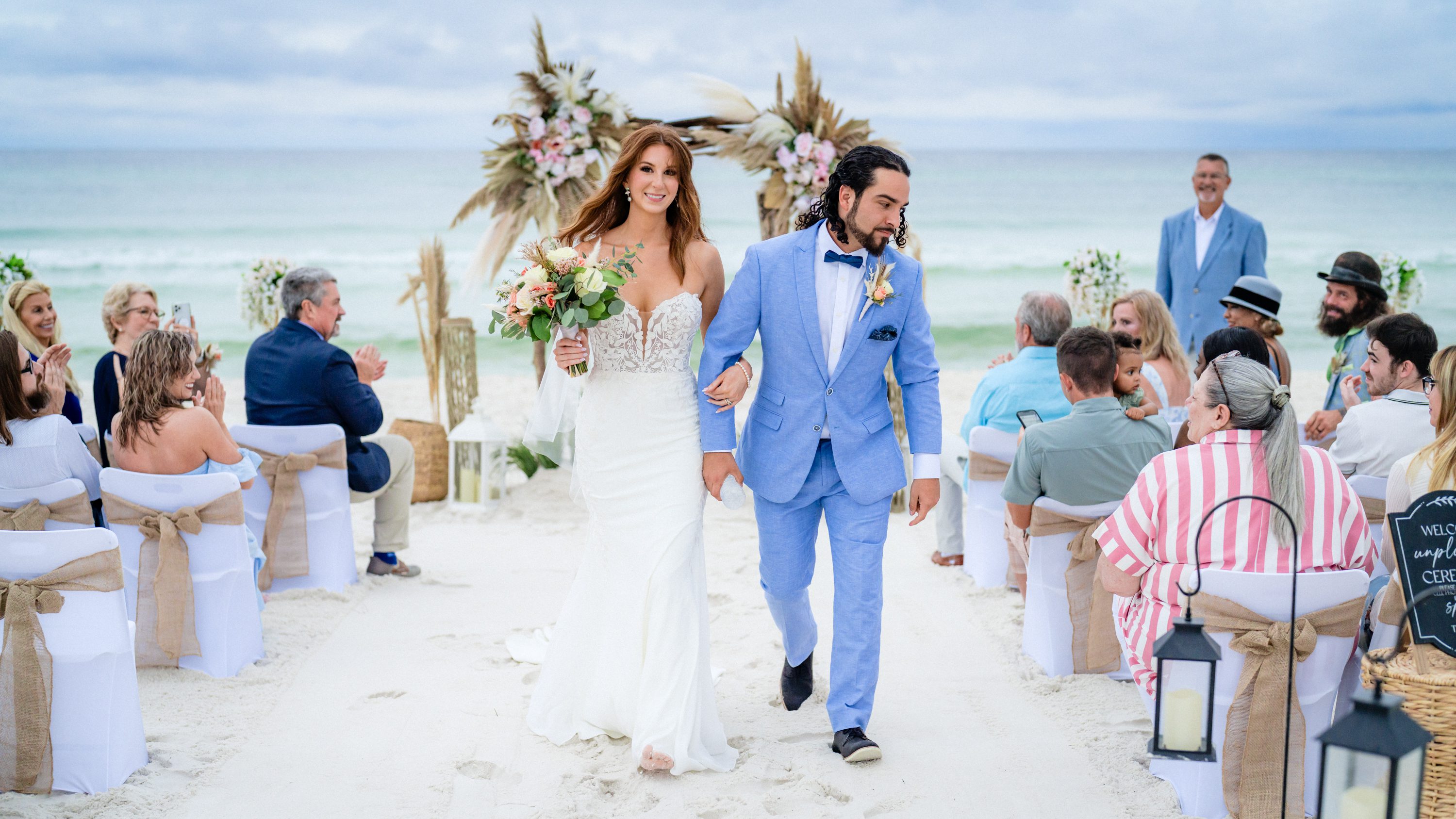 A bride and groom walking down the sandy aisle after their beach wedding ceremony.