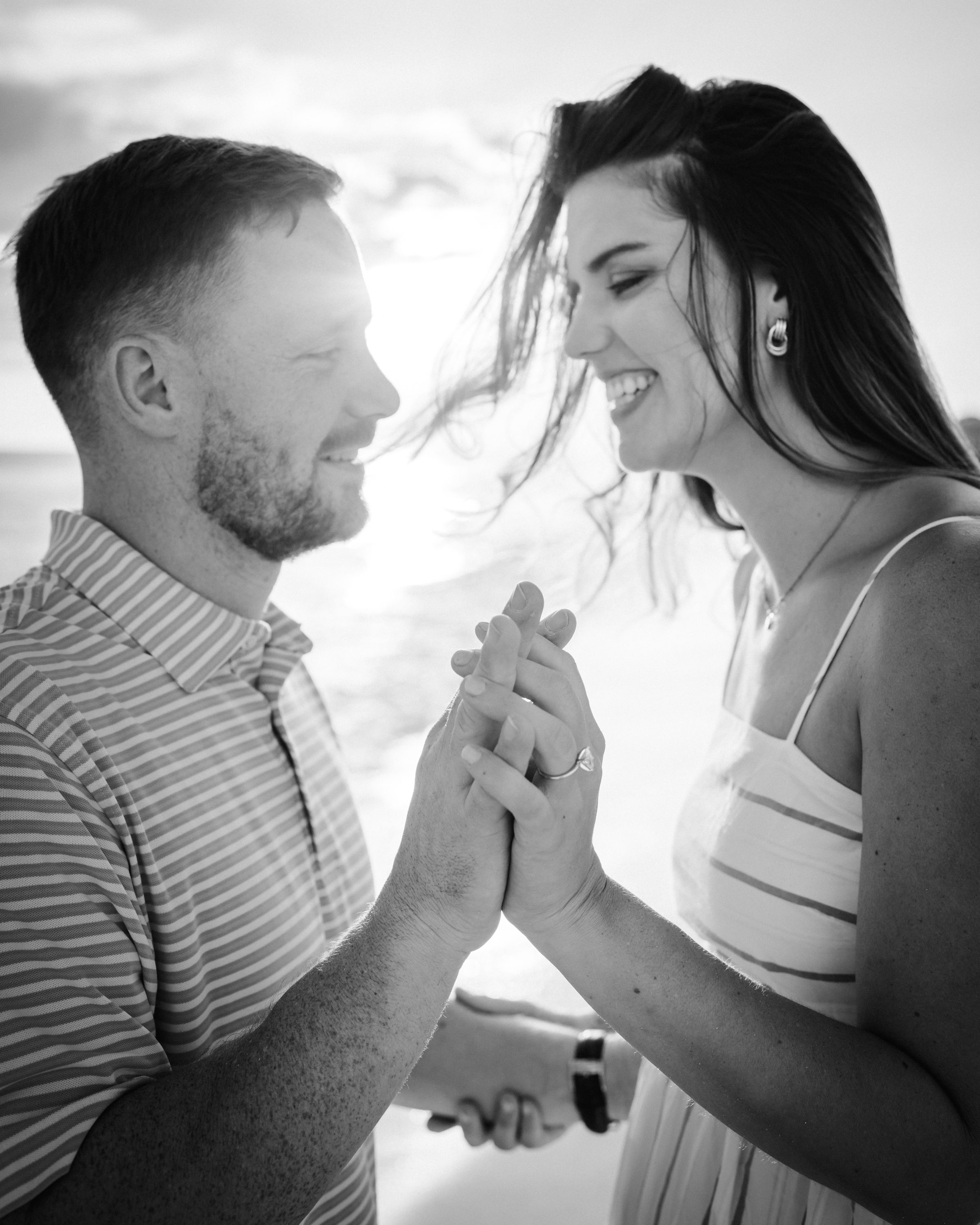 Black-and-white portrait of a smiling couple holding hands and leaning toward each other.