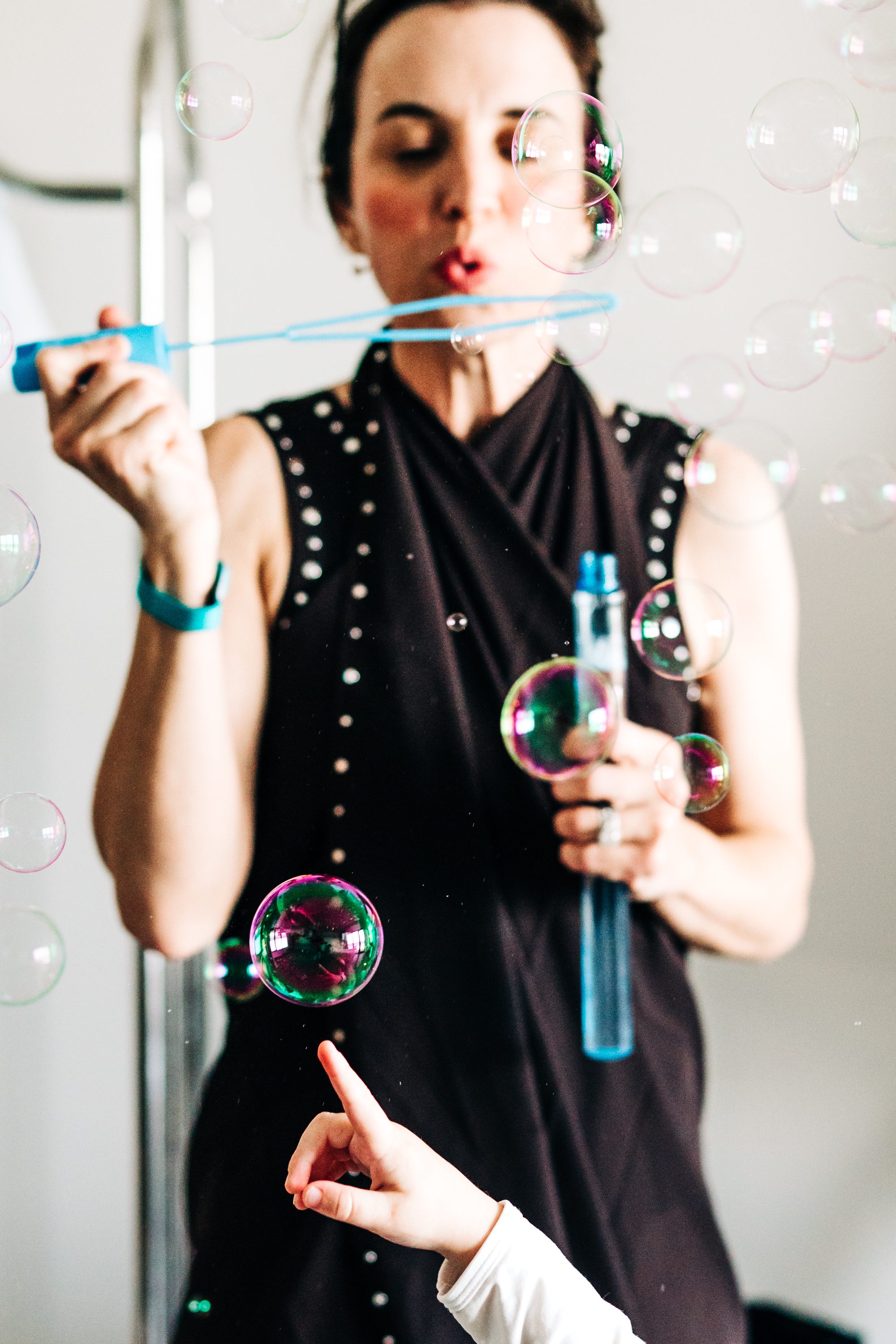 A woman blowing soap bubbles as a child reaches toward them.