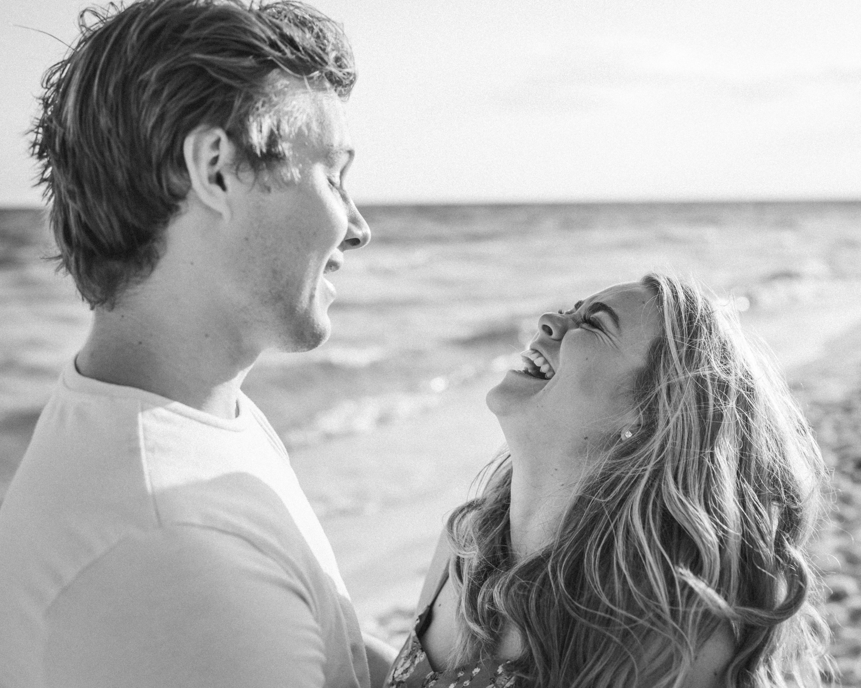 Black-and-white photograph of a couple laughing together on the beach.
